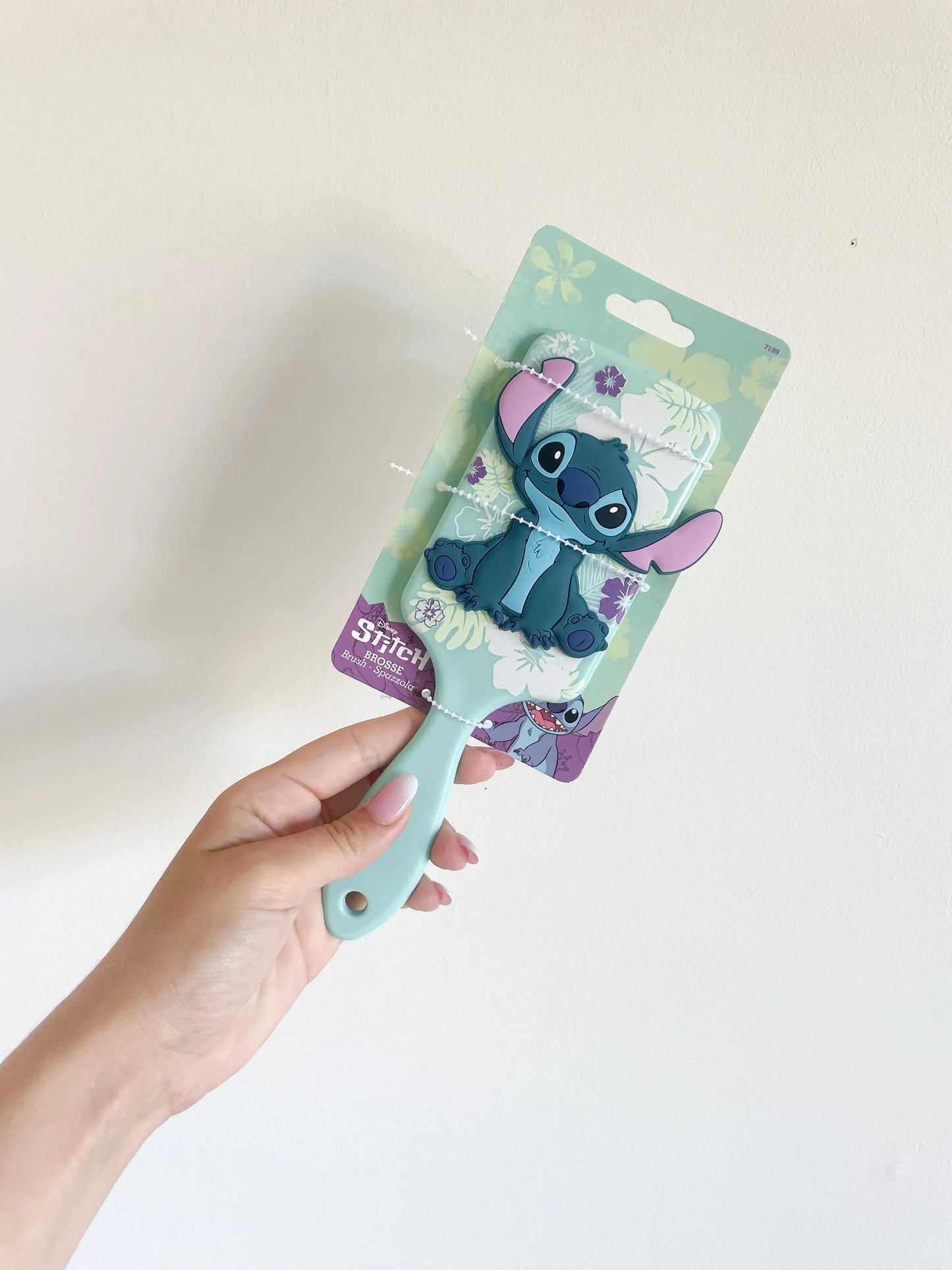 Brosse à cheveux Stitch disney de couleur bleu. Le stitch bleu en silicone 3D. Brosse tenu dans une main sur fond blanc.