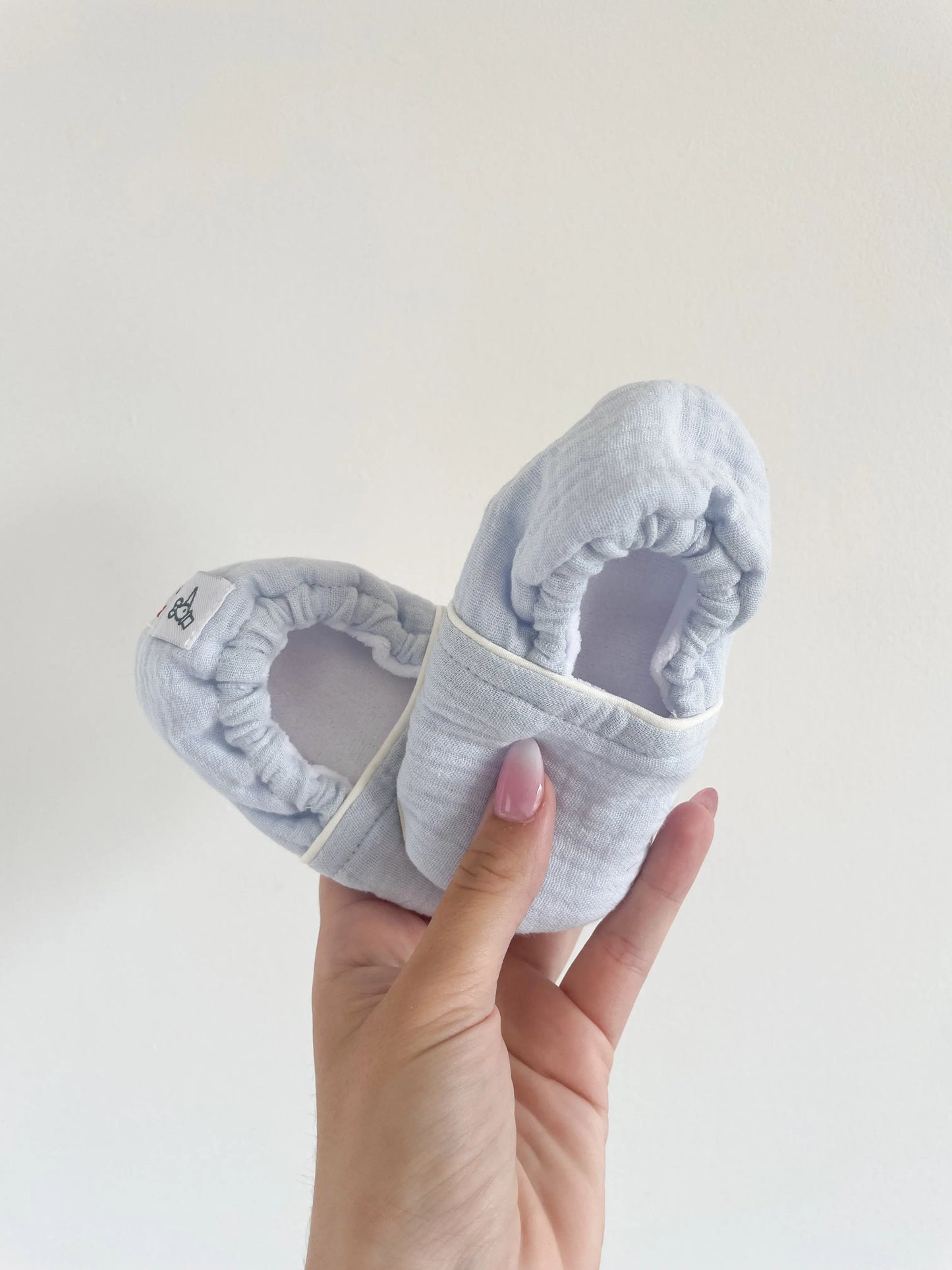 Chaussons souples bébé bleu glacé modèle Artic, tenus en main, semelle effet cuir grainé