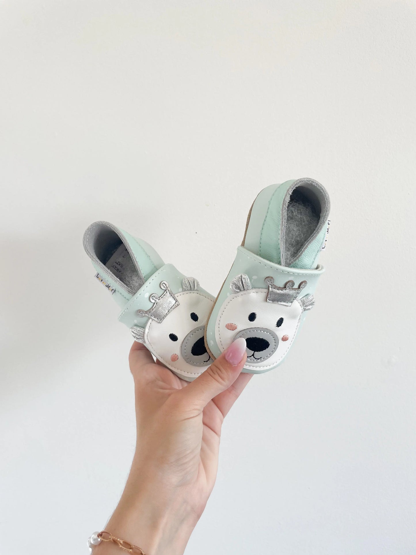 Chaussons souples bébé avec imprimés ours polaire roi de couleurs bleu, tenus a la main sur fond blanc