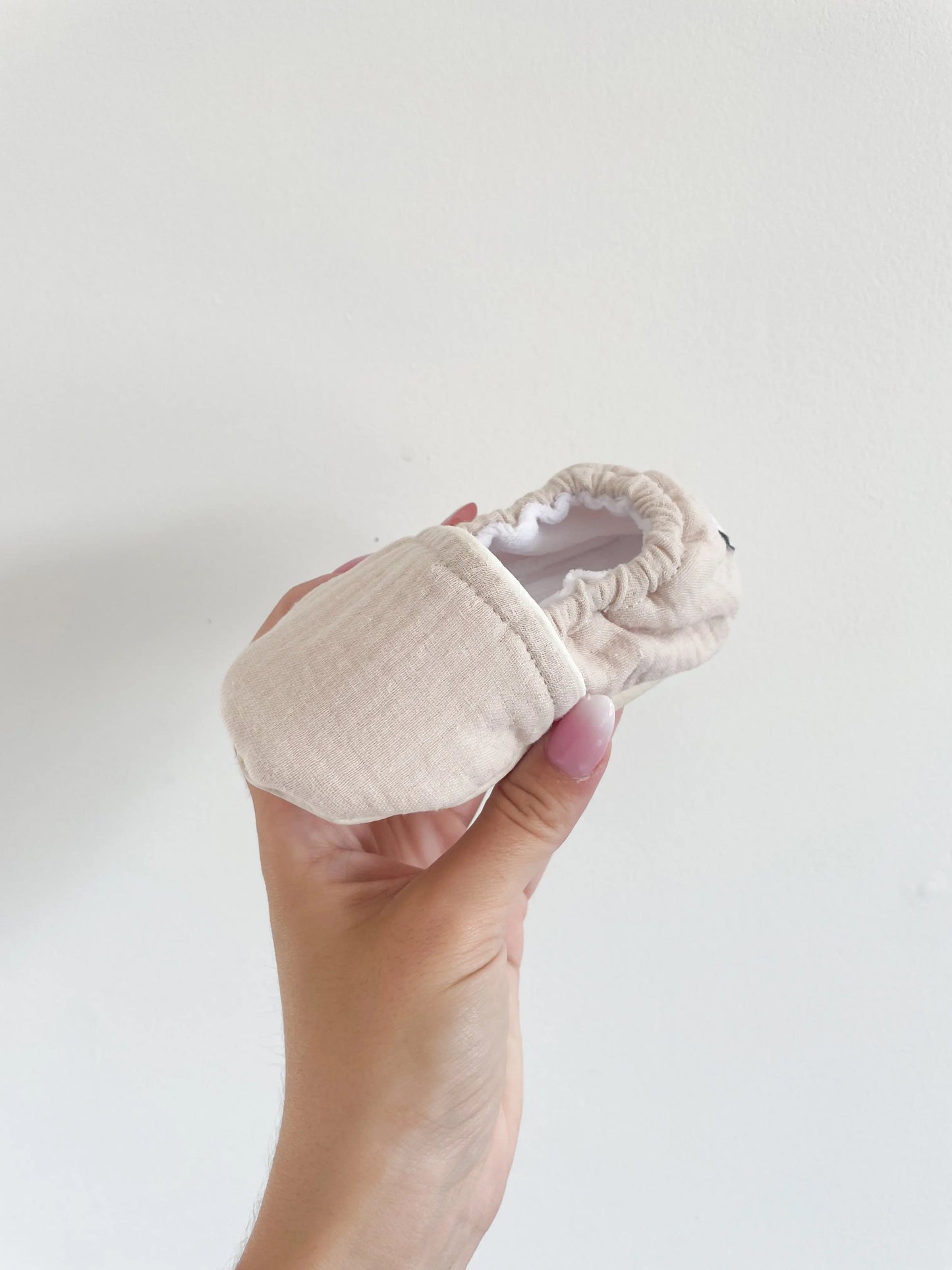 Chaussons souples sable bébé posés sur la main, tissu doux et souple adapté aux petits pieds