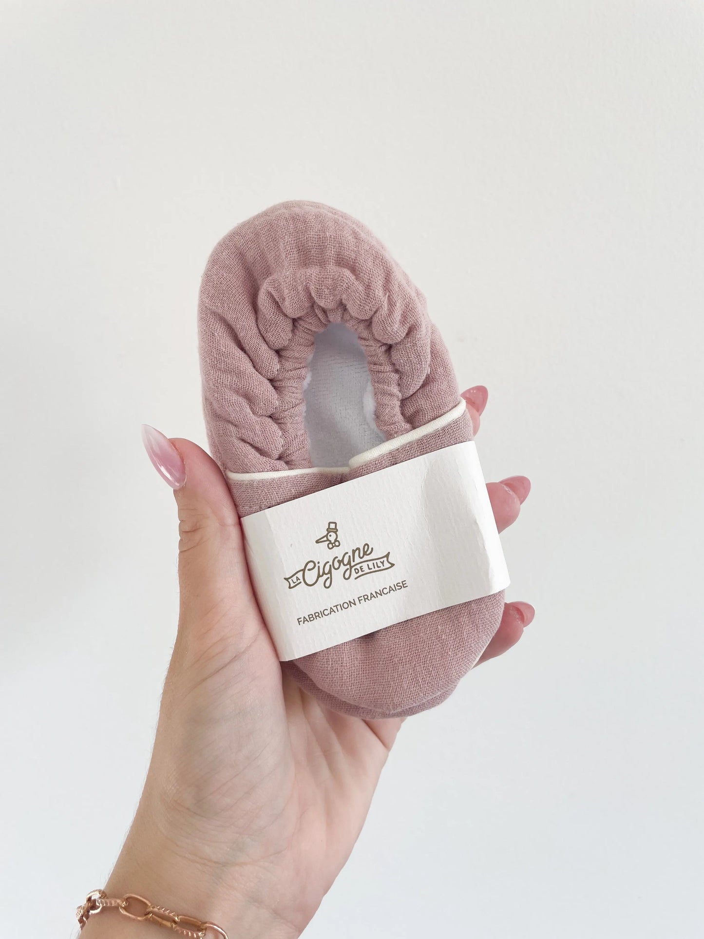 Chaussons bébé en tissu vieux rose avec semelle souple, vue du dessus sur la texture du cuir grainé et le packaging little cigogne