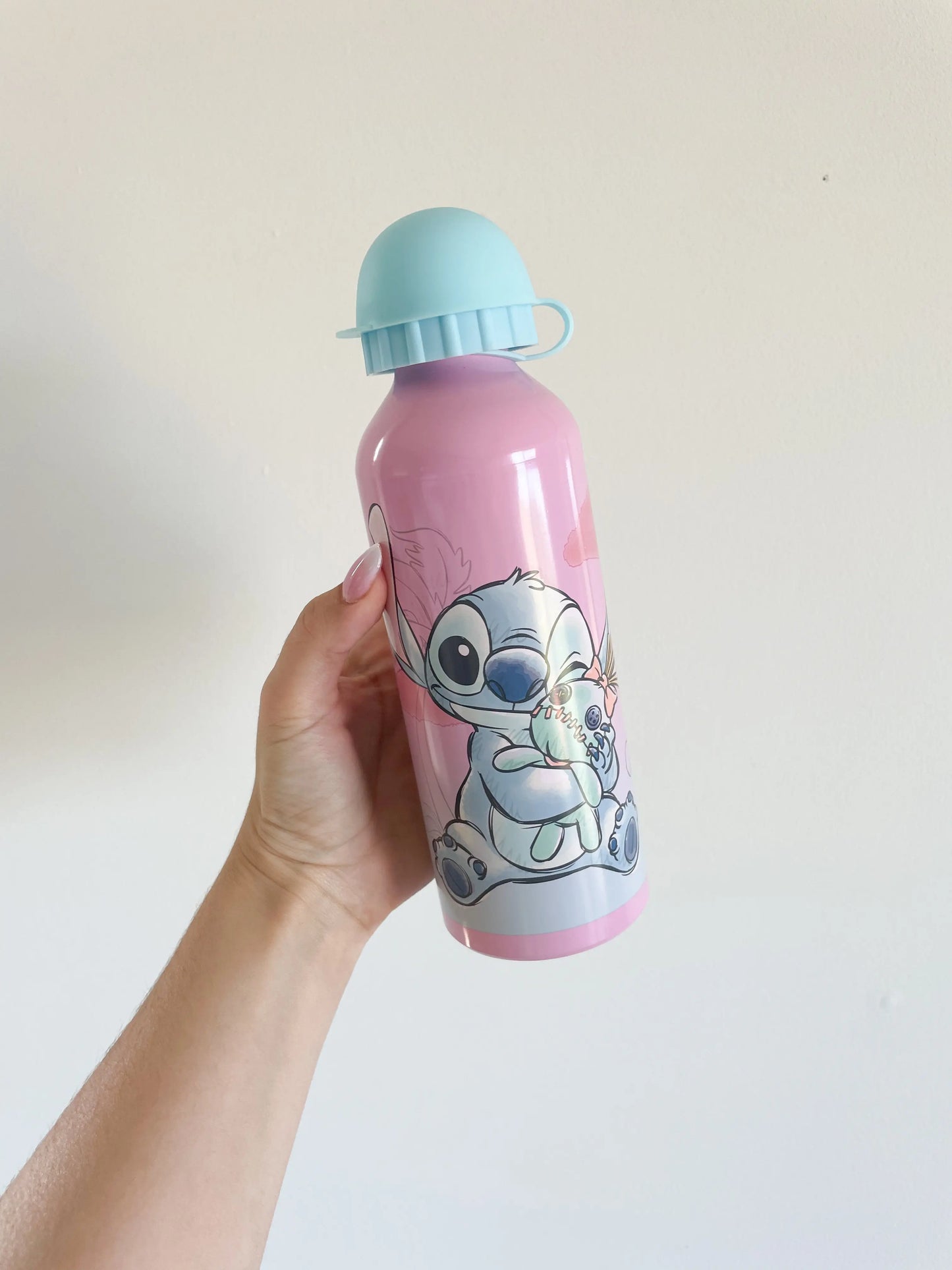 La gourde stitch rose fille disney avec stitch dessus. Bouchon bleu clair. Gourde dans une main sur fond blanc