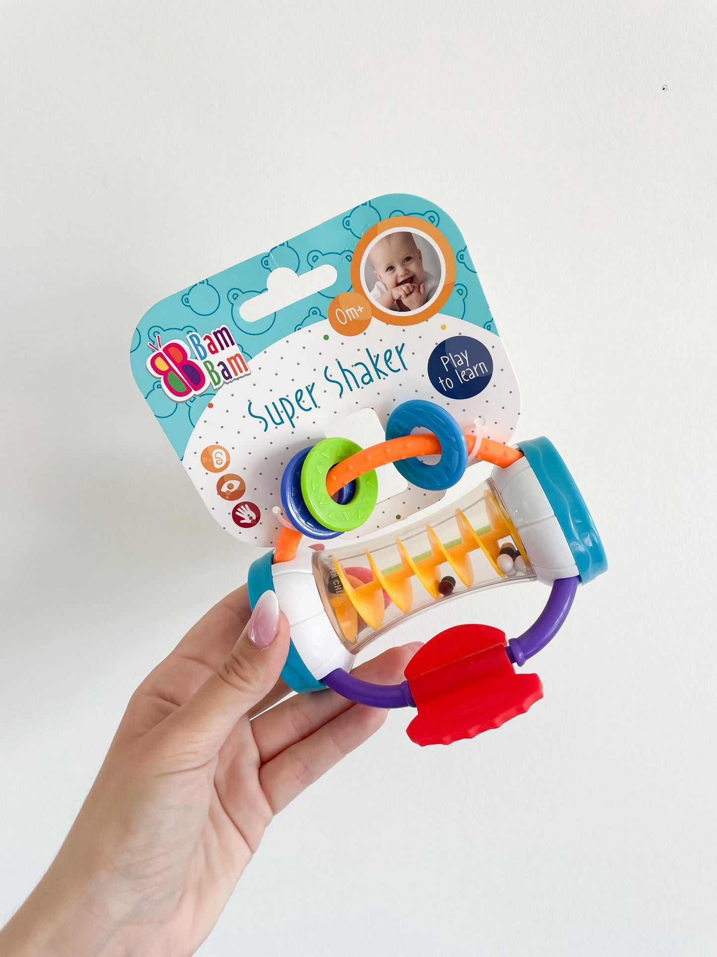 Hochet bébé multicolore incliné – vue de face tenu a la main sur fond blanc