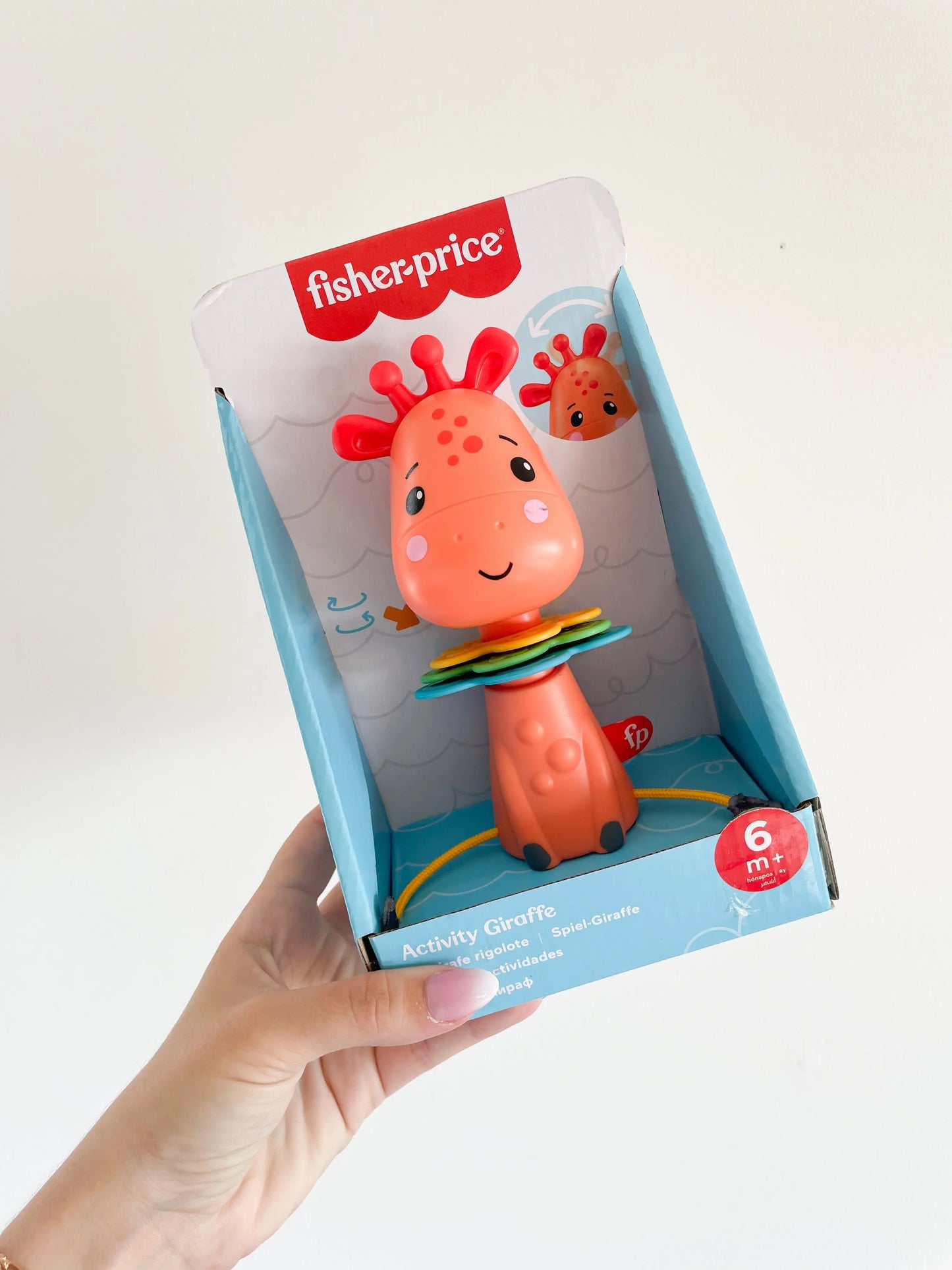 Jouet girafe rigolote Fisher-Price dans sa boîte, tenue à la main sur fond blanc – jouet d’éveil bébé dès 6 mois