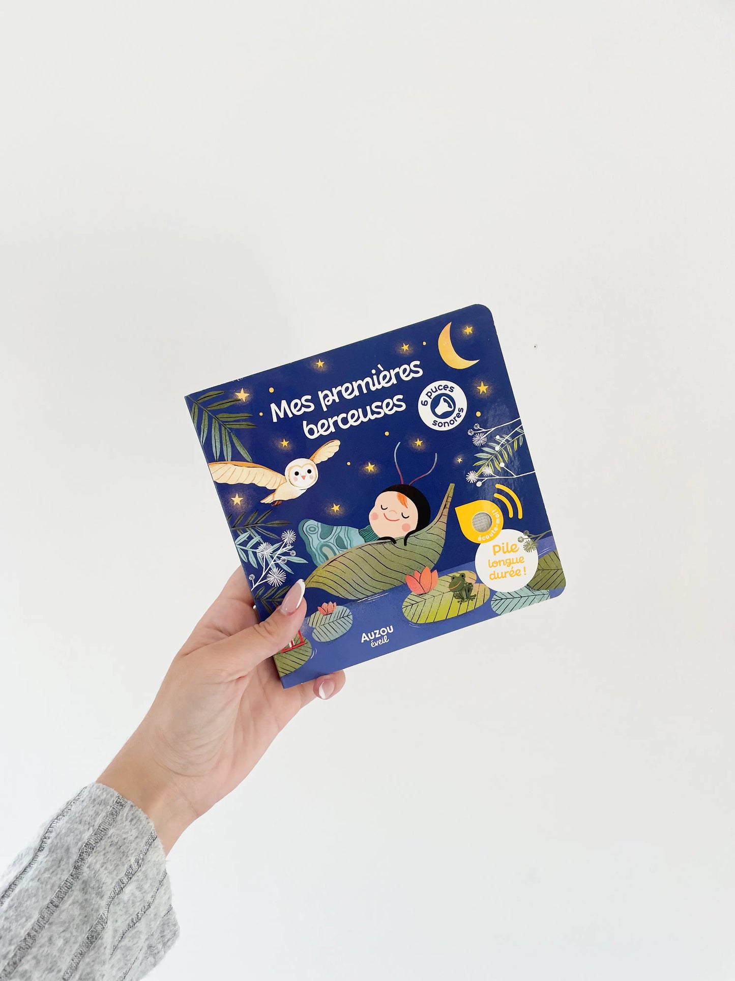 Livre sonore - Mes premières berceuses pour bébé dès 1 an. Livre de couverture bleu. Livre dans une main sur fond blanc