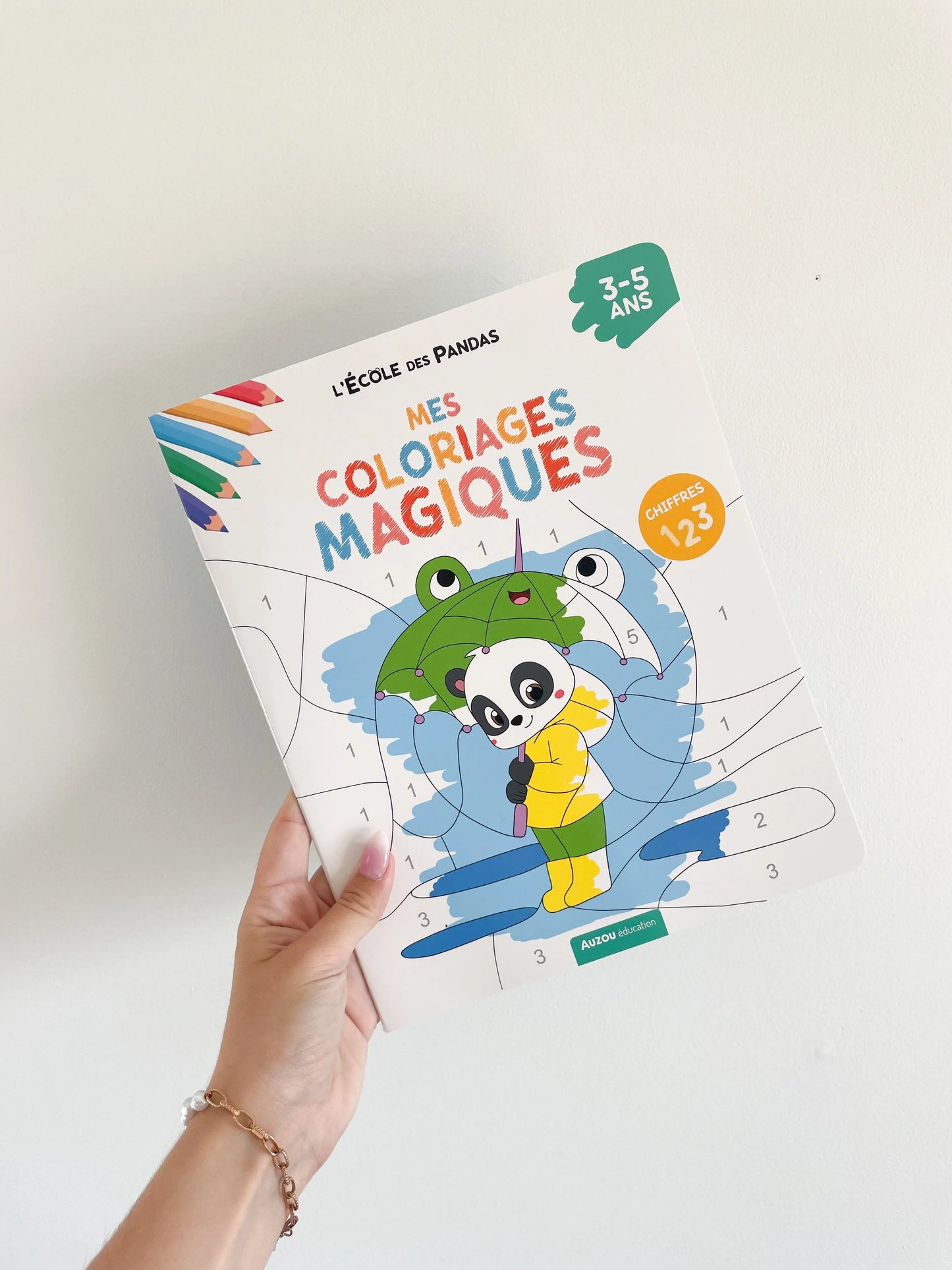 Livre coloriages magiques sur les chiffres pour enfant 3-5 ans. L'école des panda. Page de couverture. Livre dans une main sur un fond blanc