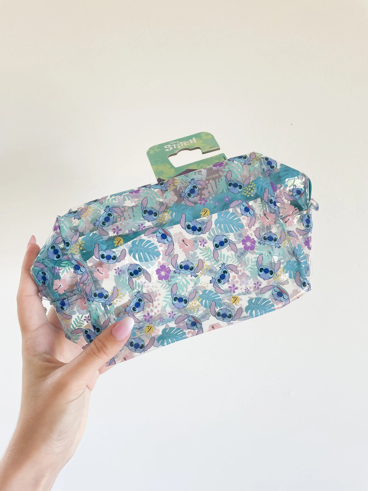 Trousse de toilette Stitch disney transparente et bleu avec pleins de petit stitch. Trousse de beauté enfant pris dans une main sur fond blanc