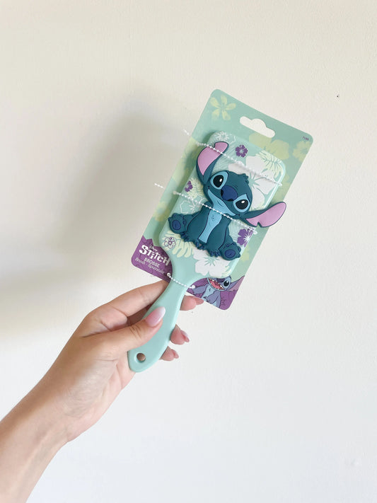 Brosse à cheveux Stitch disney de couleur bleu. Le stitch bleu en silicone 3D. Brosse tenu dans une main sur fond blanc.