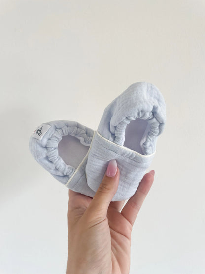 Chaussons souples bébé bleu glacé modèle Artic, tenus en main, semelle effet cuir grainé