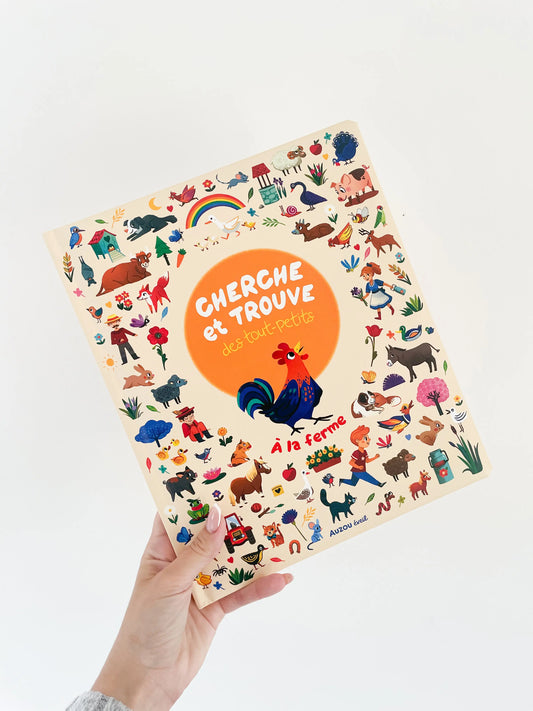 Livre pour bébé cherche et trouve des tout petits - A la ferme. Page de couverture avec des petits éléments. Livre dans une main sur fond blanc