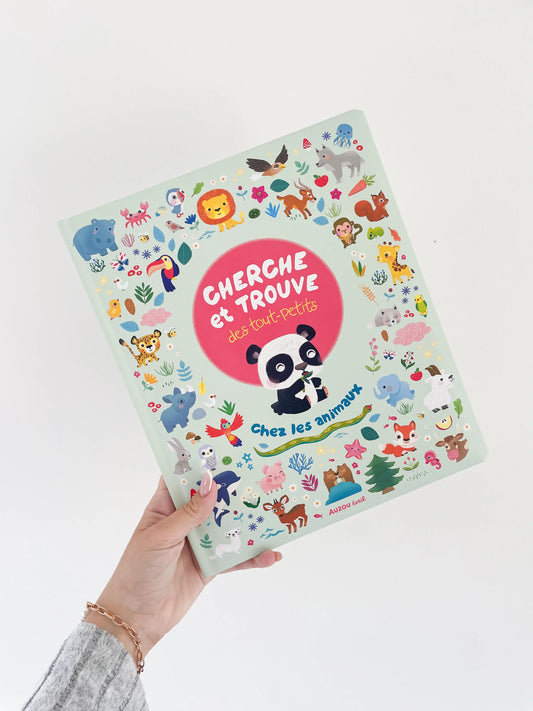 Livre cherche et trouve des tout petits - Chez les animaux. Page de couverture avec un panda et des petit élements. Livre dans une main sur un fond blanc.