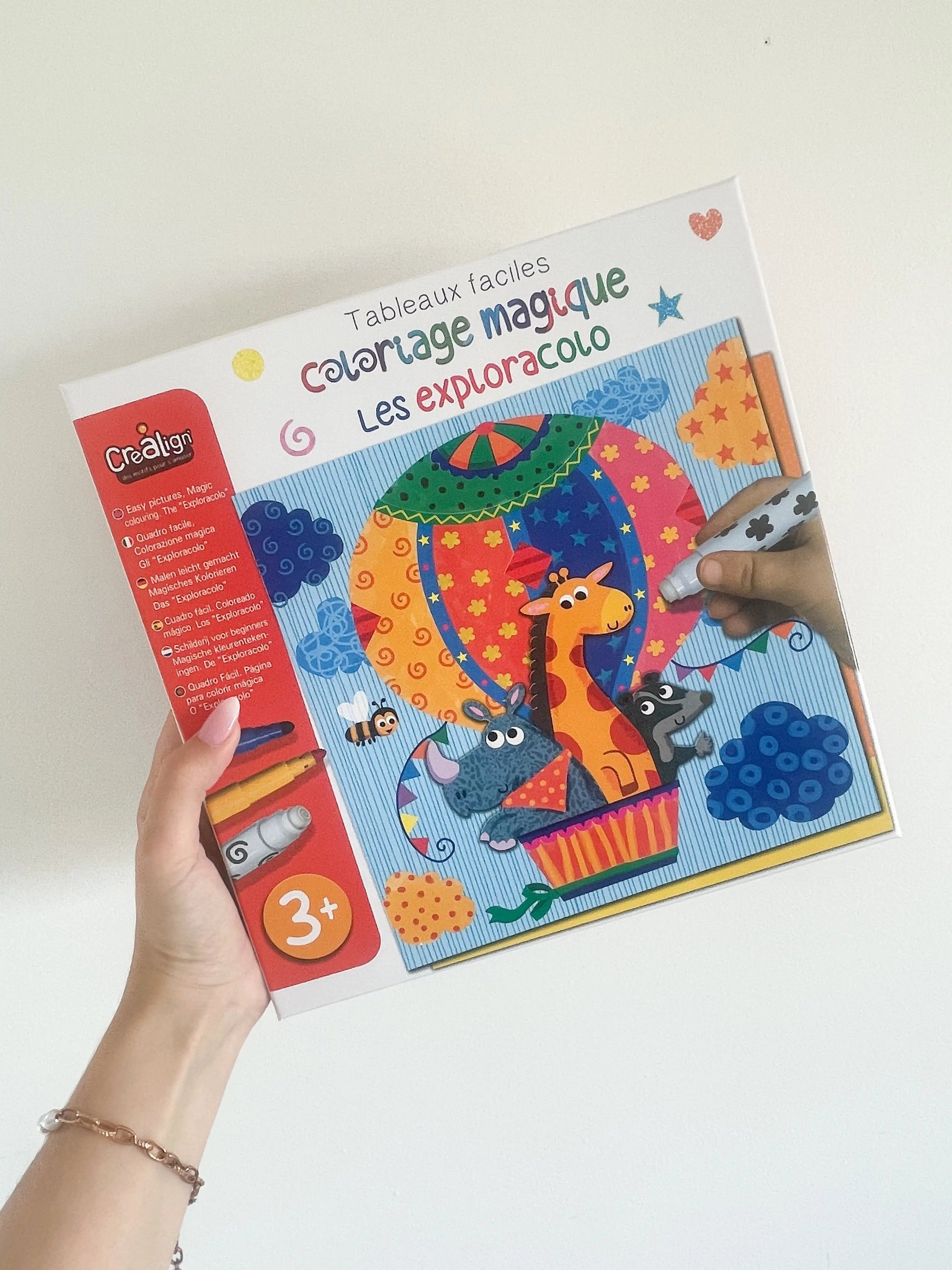 Le coloriage magique Les Exploracolo, tenu à la main sur fond blanc, conçu pour enfants dès 3 ans.