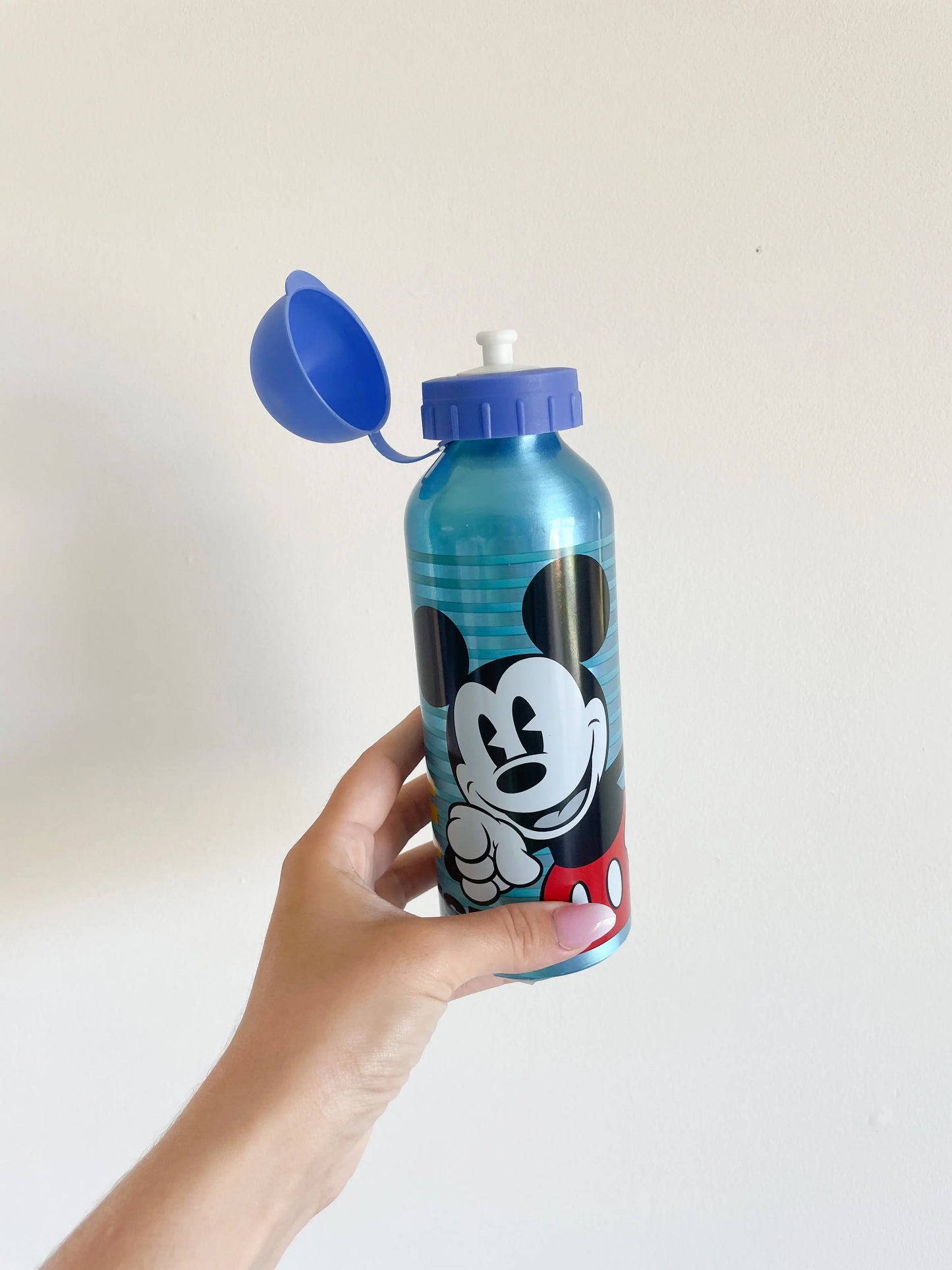 Gourde Mickey pour enfant avec bouchon  bleu ouvert. Avec main qui tient la gourde sur un fond blanc