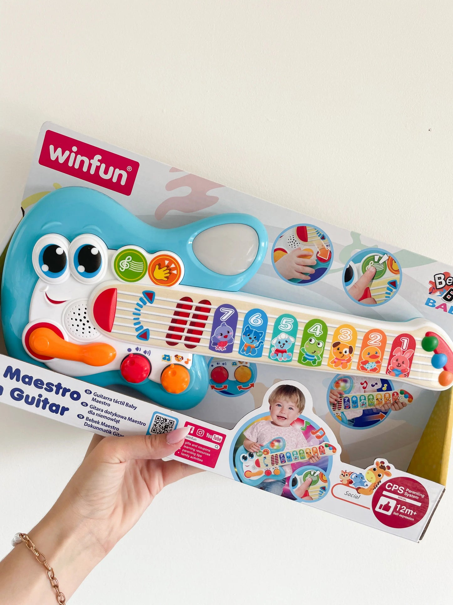 Guitare électronique tactile pour bébé 1 an. Avec bruits d'animaux dans son packaging. Guitare dans une main sur un fond blanc