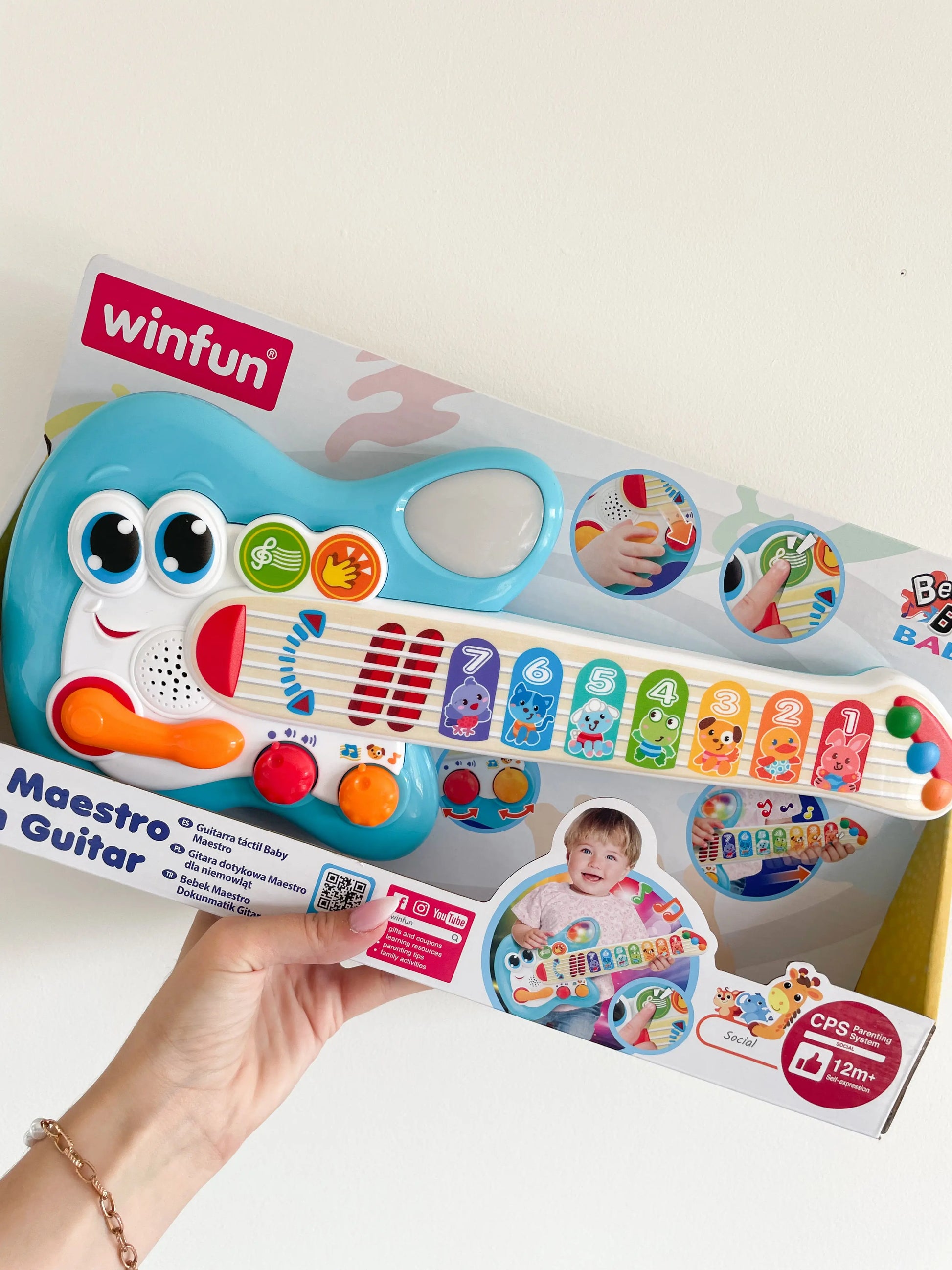 Guitare électronique tactile pour bébé 1 an. Avec bruits d'animaux dans son packaging. Guitare dans une main sur un fond blanc