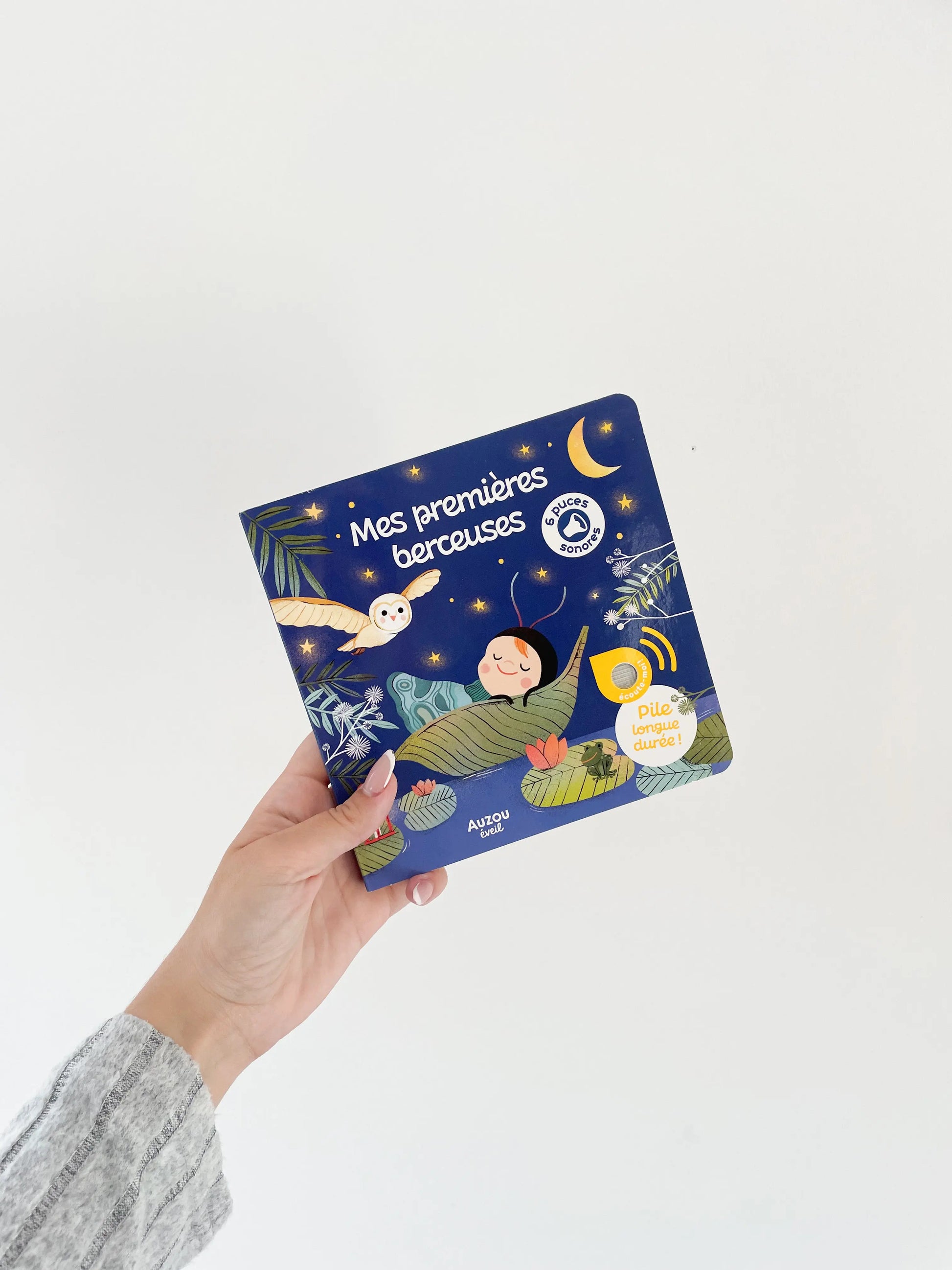 Livre sonore - Mes premières berceuses pour bébé dès 1 an. Livre de couverture bleu. Livre dans une main sur fond blanc