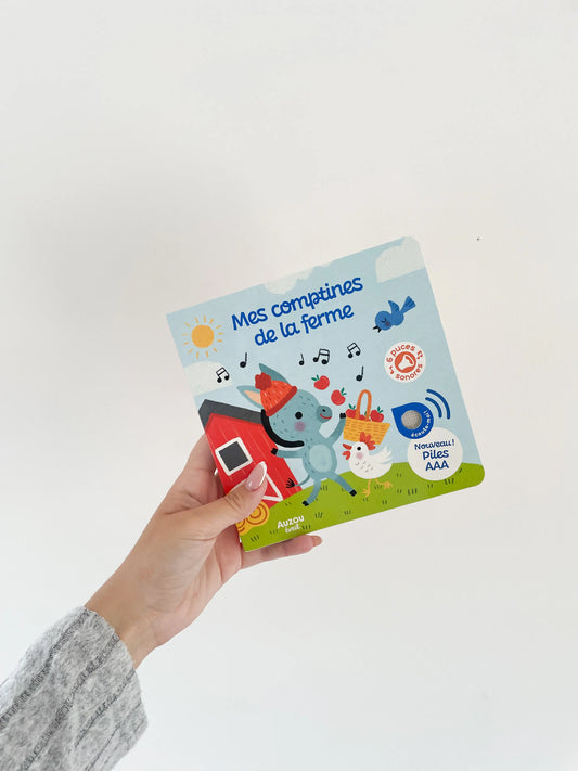 Livre sonore musique bébé - Mes comptines de la ferme. Page de couverture. livre dans une main sur fond blanc