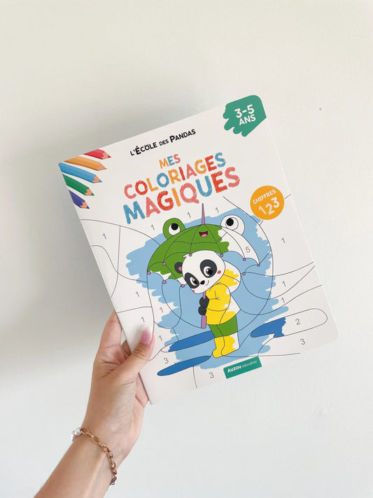 Livre coloriages magiques sur les chiffres pour enfant 3-5 ans. L'école des panda. Page de couverture. Livre dans une main sur un fond blanc