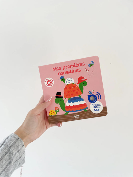 Mes premières comptines - Livre sonore pour bébé dès 1an. Livre dans une main sur fond blanc
