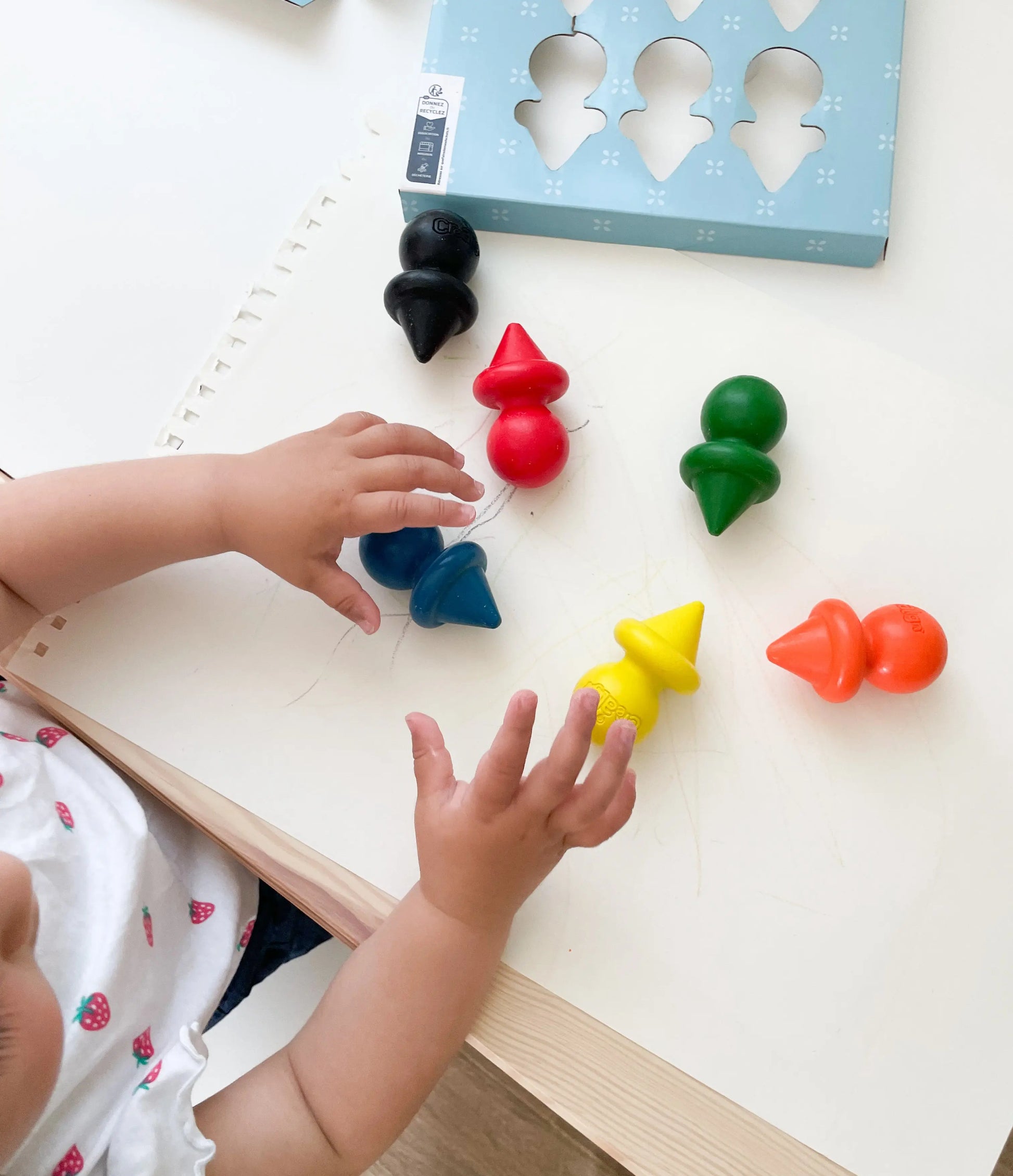 Enfant utilisant plusieurs crayons de cire pour bébé, activité de coloriage libre sur feuille
