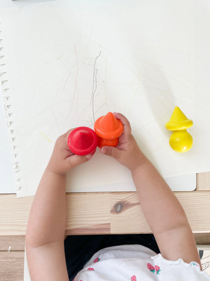 Crayons bébé ergonomiques multicolores, dans la main de bébé avec une feuille blanche derrière 
