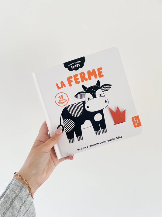 Livre noir et blanc bébé sur la ferme  Mes premiers flaps -Page de couverture. Livre dans une main sur fond blanc