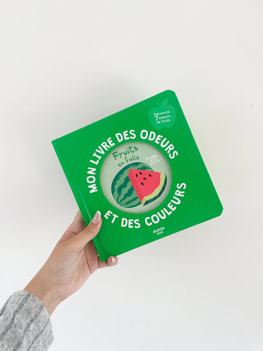 Mon livre des odeurs et des couleurs - Fruits en folie. Page de couverture verte avec pastèque. Livre imagier et odeurs. Dès 1an. Livre dans une main sur fond blanc.